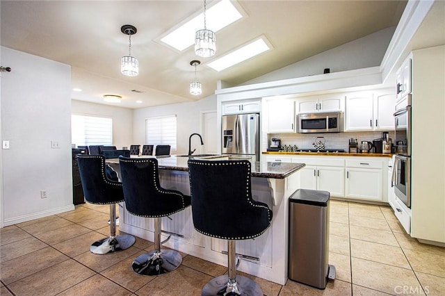 kitchen featuring pendant lighting, a kitchen island with sink, white cabinets, appliances with stainless steel finishes, and a breakfast bar area