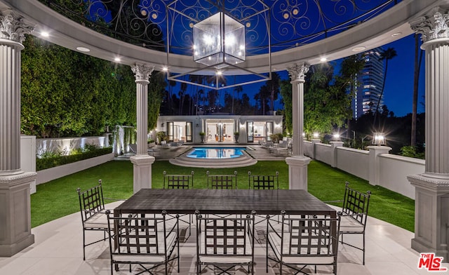 patio at night featuring a yard and a fenced in pool