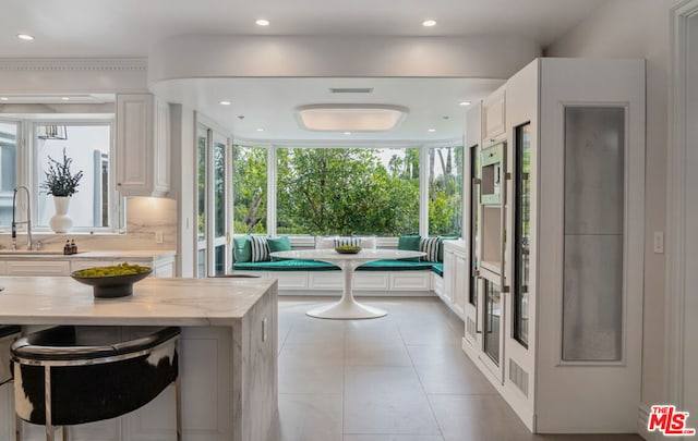 interior space featuring a breakfast bar, light stone countertops, breakfast area, and white cabinetry