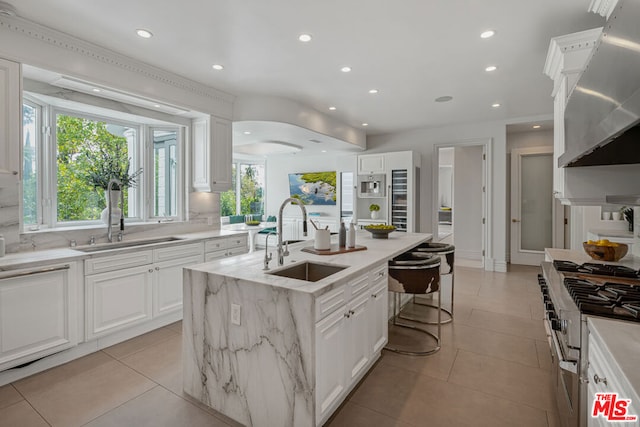 kitchen featuring a kitchen island with sink, stainless steel gas stove, a healthy amount of sunlight, sink, and white cabinets