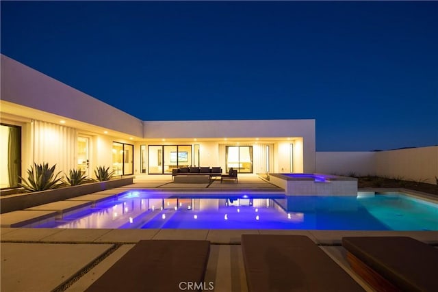 pool at night featuring outdoor lounge area, a patio area, and an in ground hot tub