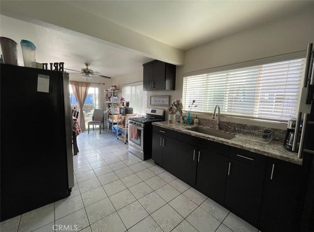 kitchen with black refrigerator, ceiling fan, sink, stainless steel range with gas cooktop, and light tile patterned flooring