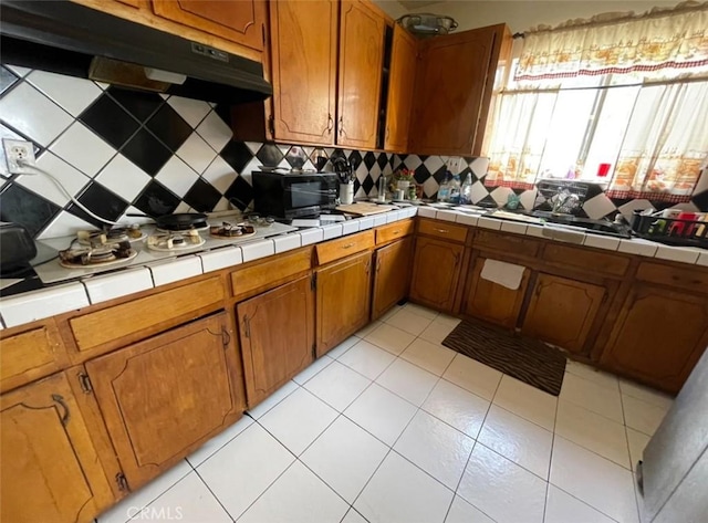 kitchen with tile countertops, light tile patterned flooring, stainless steel gas cooktop, and tasteful backsplash