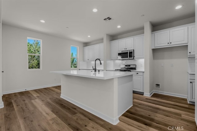 kitchen featuring appliances with stainless steel finishes, a kitchen island with sink, white cabinetry, and dark hardwood / wood-style flooring