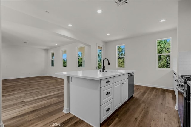 kitchen with a center island with sink, appliances with stainless steel finishes, white cabinetry, hardwood / wood-style flooring, and sink