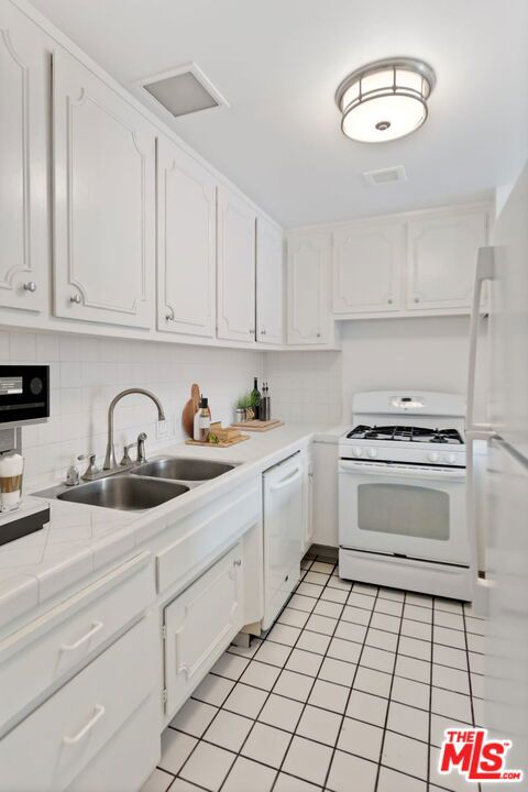 kitchen with light tile flooring, sink, white appliances, and white cabinets