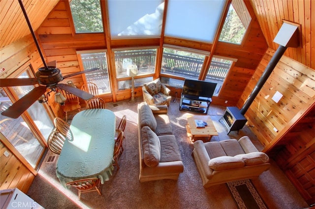 carpeted living room with a wood stove, high vaulted ceiling, and a healthy amount of sunlight