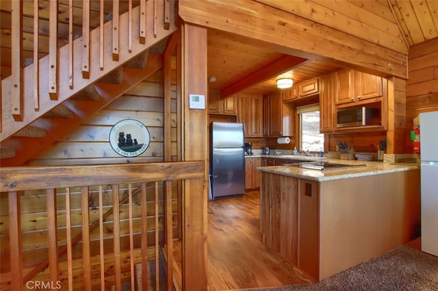 kitchen featuring kitchen peninsula, wood walls, light hardwood / wood-style floors, and stainless steel appliances