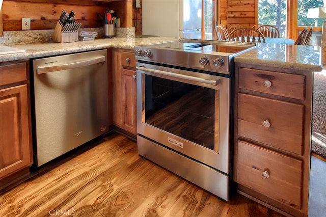 kitchen featuring kitchen peninsula, appliances with stainless steel finishes, light wood-type flooring, light stone counters, and wooden walls