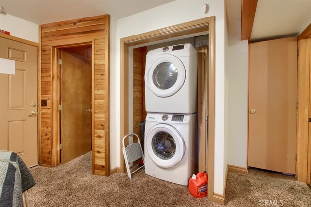 clothes washing area with wood walls, stacked washing maching and dryer, and carpet floors