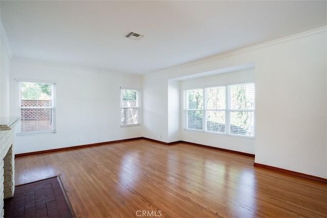 spare room featuring hardwood / wood-style floors, a brick fireplace, ornamental molding, and a healthy amount of sunlight