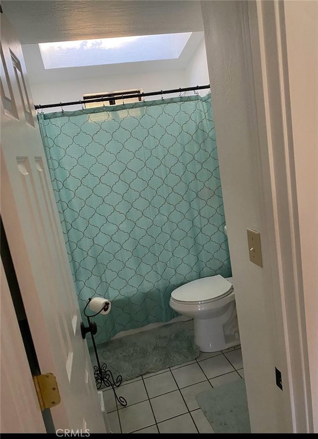 bathroom featuring toilet, a skylight, a shower with curtain, and tile patterned flooring