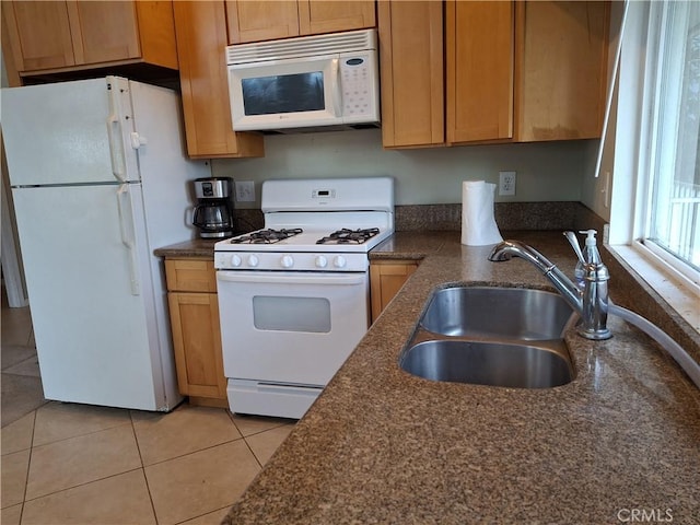 kitchen with light tile patterned flooring, white appliances, dark stone counters, and sink