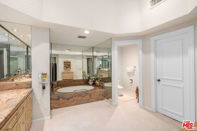 bathroom with tiled bath, vanity, and toilet