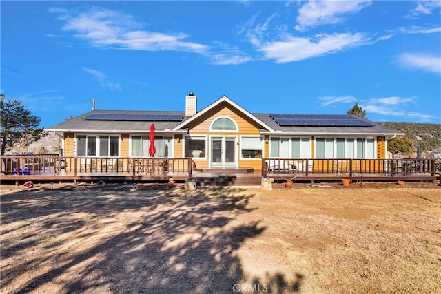 rear view of house featuring solar panels and a wooden deck