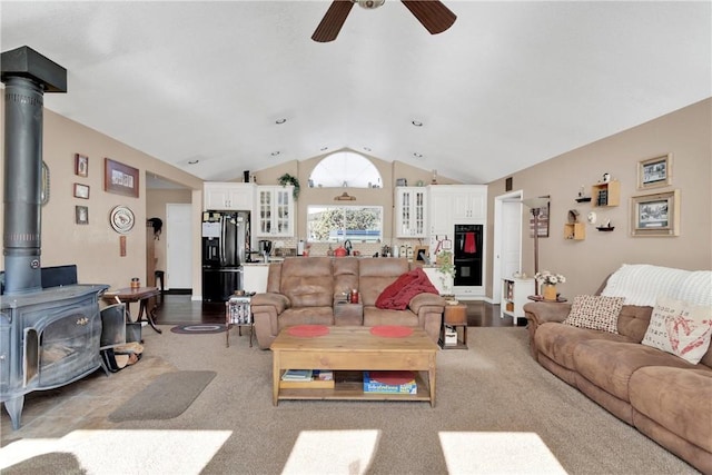 living room featuring ceiling fan, a wood stove, light hardwood / wood-style flooring, and vaulted ceiling