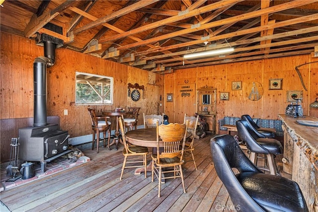 dining area featuring a wood stove, wood walls, hardwood / wood-style floors, and vaulted ceiling