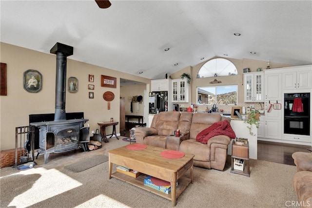 carpeted living room featuring a wood stove and vaulted ceiling