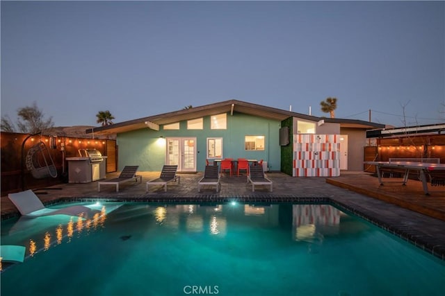 pool at dusk with french doors, grilling area, and area for grilling