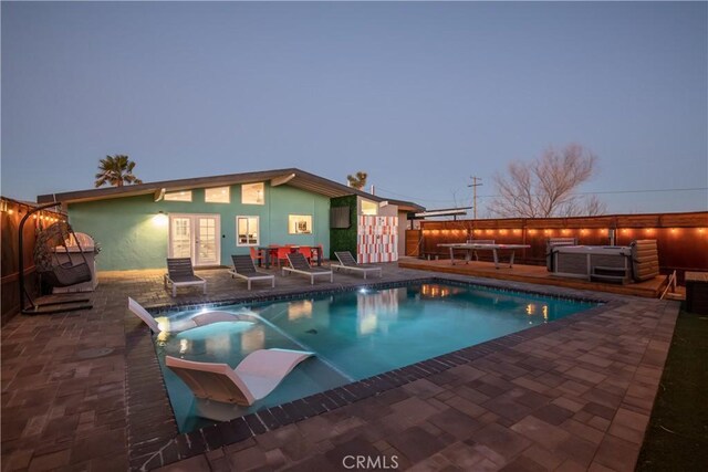 pool at dusk with a patio area, an outdoor living space, and french doors