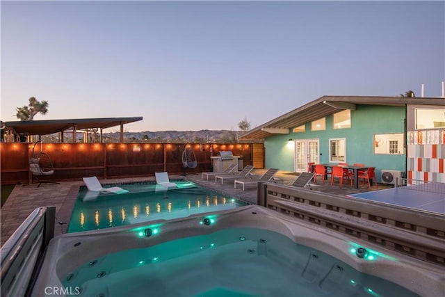 pool at dusk featuring a mountain view, an outdoor hot tub, french doors, and a patio