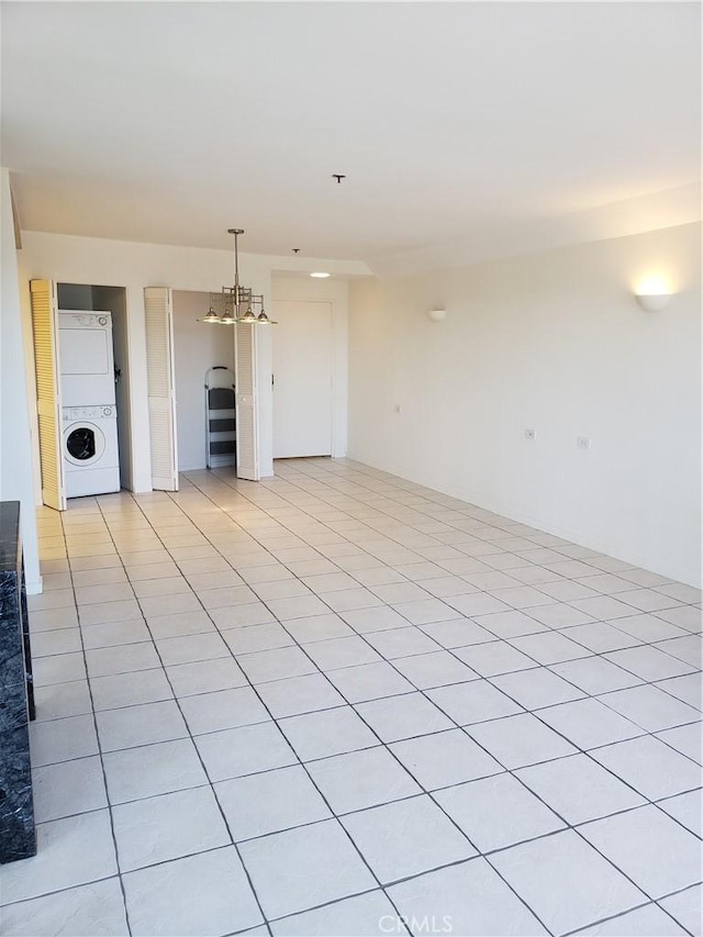 unfurnished living room with an inviting chandelier, light tile patterned floors, and stacked washer and clothes dryer