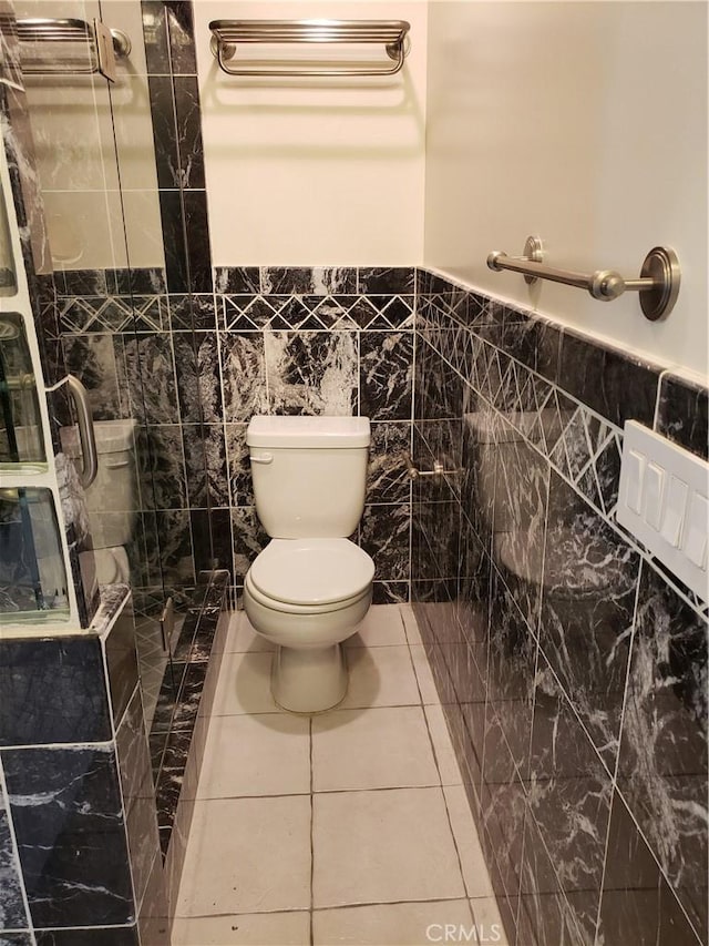 bathroom with a tile shower, tile patterned floors, tile walls, and toilet