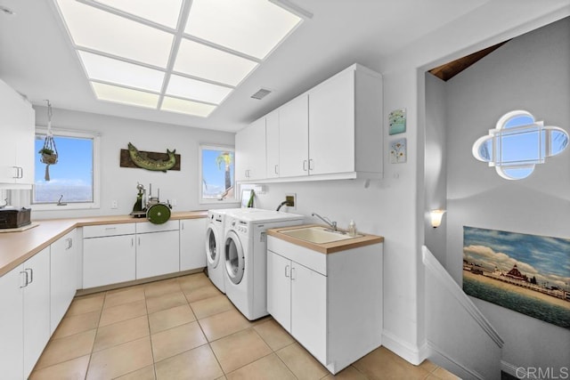 clothes washing area featuring light tile patterned floors, visible vents, a sink, washer and dryer, and cabinet space
