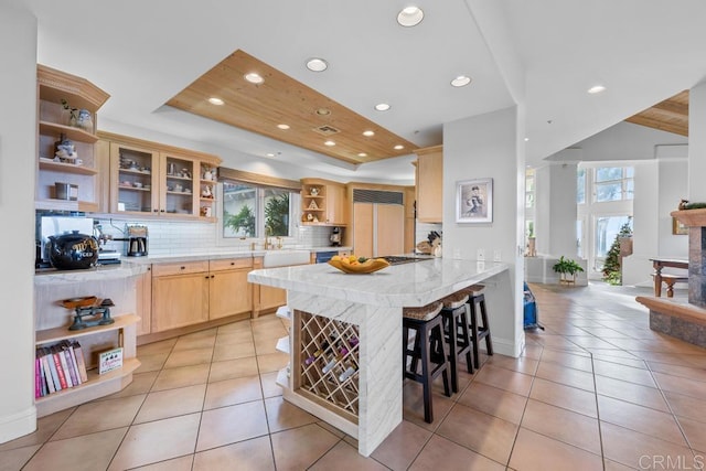 kitchen with light tile patterned floors, kitchen peninsula, light brown cabinetry, a kitchen bar, and decorative backsplash