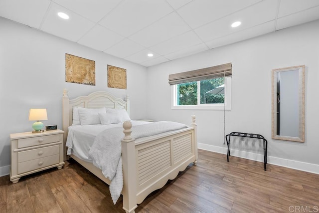 bedroom with baseboards, recessed lighting, a drop ceiling, and wood finished floors