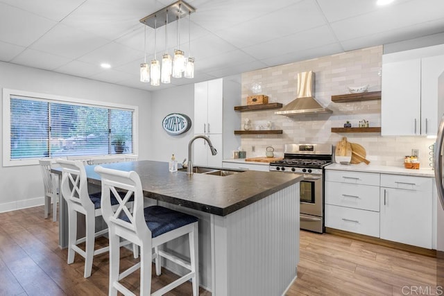 kitchen featuring a kitchen bar, stainless steel range with gas cooktop, wall chimney exhaust hood, and open shelves