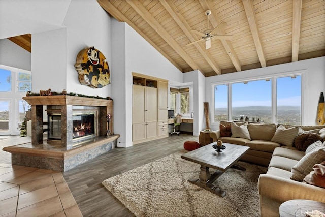 living area featuring high vaulted ceiling, ceiling fan, beamed ceiling, a fireplace, and wooden ceiling