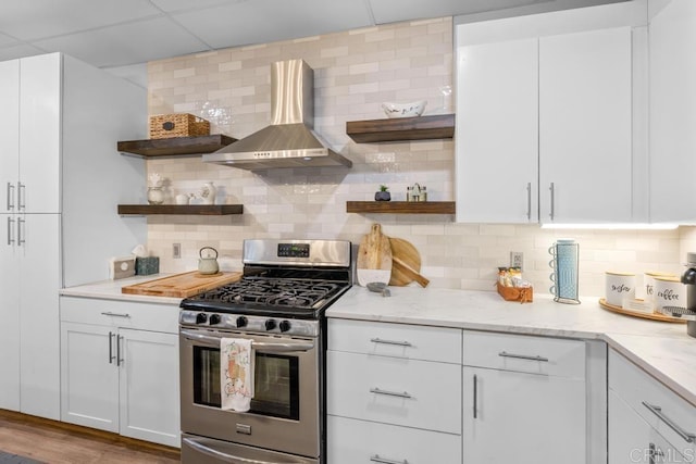 kitchen with decorative backsplash, white cabinetry, stainless steel gas range oven, and wall chimney range hood