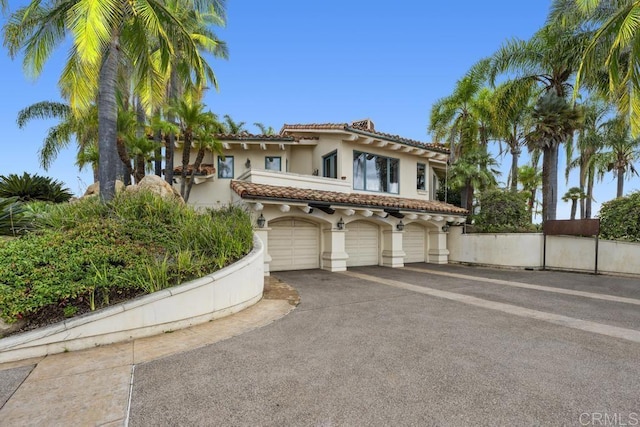 mediterranean / spanish house featuring stucco siding, driveway, an attached garage, a tiled roof, and fence