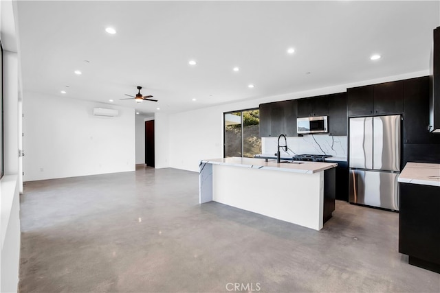 kitchen with an island with sink, sink, appliances with stainless steel finishes, decorative backsplash, and a wall unit AC