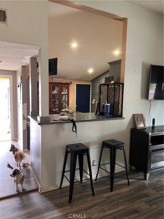 kitchen with a kitchen breakfast bar, kitchen peninsula, a textured ceiling, and dark hardwood / wood-style floors