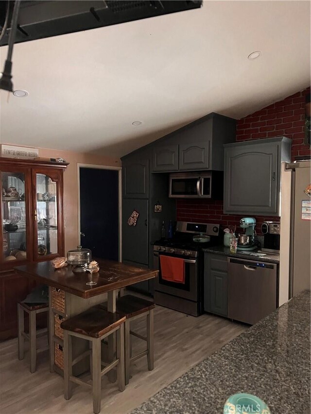 kitchen featuring gray cabinetry, vaulted ceiling, a kitchen bar, appliances with stainless steel finishes, and light wood-type flooring