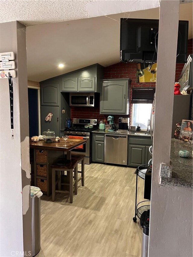 kitchen with sink, backsplash, lofted ceiling, appliances with stainless steel finishes, and light wood-type flooring