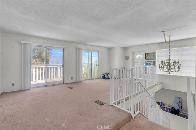 carpeted empty room with visible vents, an inviting chandelier, and a textured ceiling