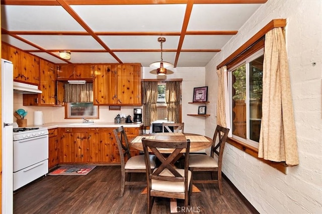 kitchen with kitchen peninsula, white gas range oven, brick wall, dark wood-type flooring, and hanging light fixtures