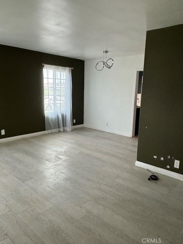 spare room featuring a notable chandelier, wood finished floors, and baseboards