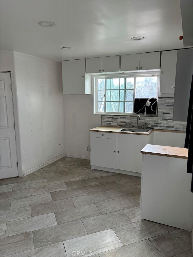 kitchen featuring light countertops, backsplash, a sink, and white cabinetry