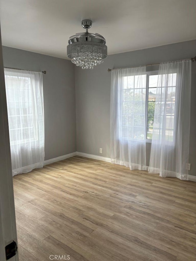 unfurnished room featuring baseboards, a chandelier, and wood finished floors