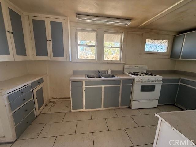 kitchen with white cabinetry, light tile patterned floors, gray cabinetry, sink, and white range with gas stovetop