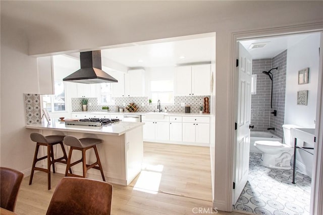 kitchen featuring kitchen peninsula, a kitchen breakfast bar, wall chimney exhaust hood, sink, and white cabinetry