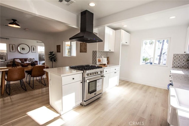 kitchen featuring white cabinetry, wall chimney range hood, high end stainless steel range oven, backsplash, and light hardwood / wood-style floors