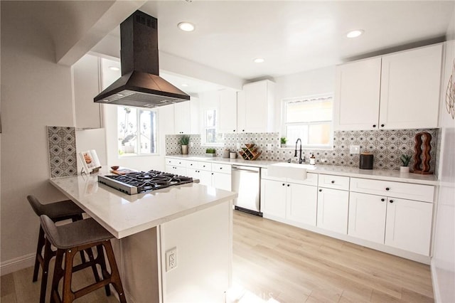 kitchen featuring sink, white cabinetry, kitchen peninsula, island exhaust hood, and stainless steel appliances