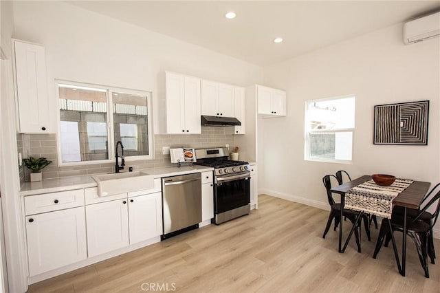 kitchen featuring appliances with stainless steel finishes, light wood-type flooring, a wall mounted AC, sink, and white cabinetry