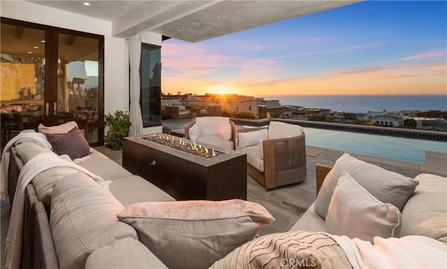 balcony at dusk featuring a water view, an outdoor living space with a fire pit, and a patio area