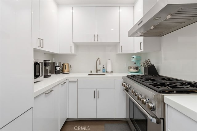 kitchen featuring white cabinets, high end stainless steel range oven, wall chimney exhaust hood, and sink